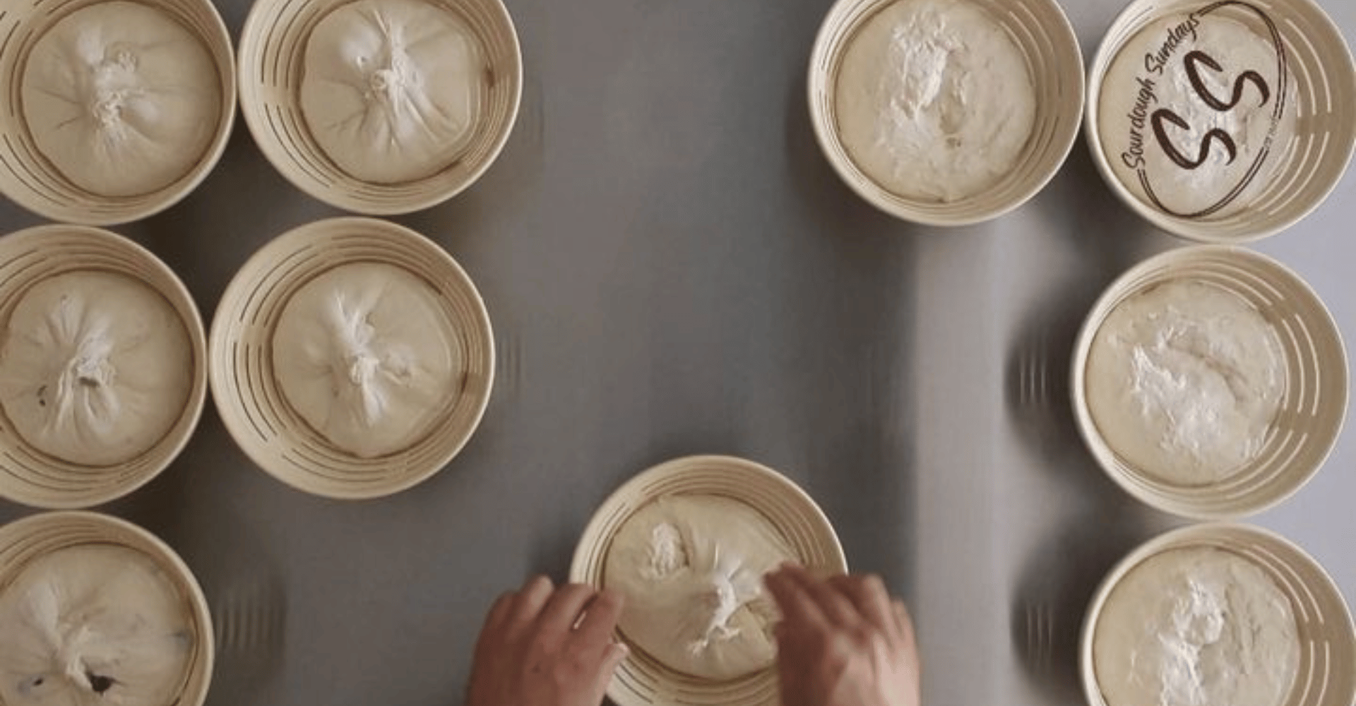 Hands arranging baking bannetons on a gray surface