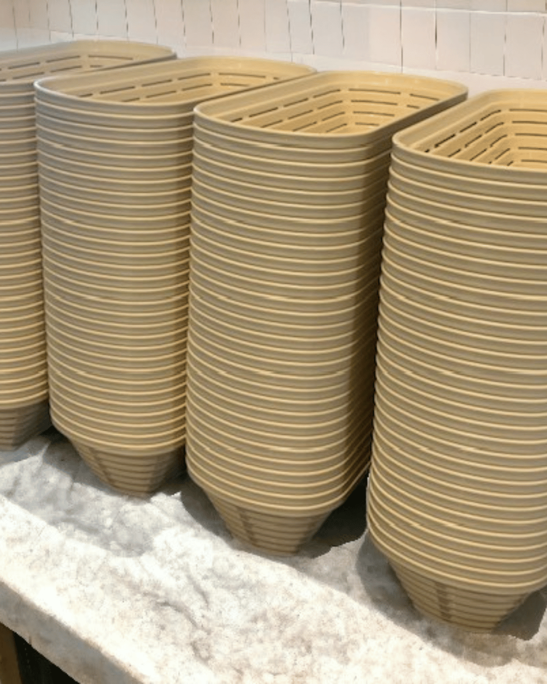 Stacks of beige woven baskets on a white surface with a tiled wall background